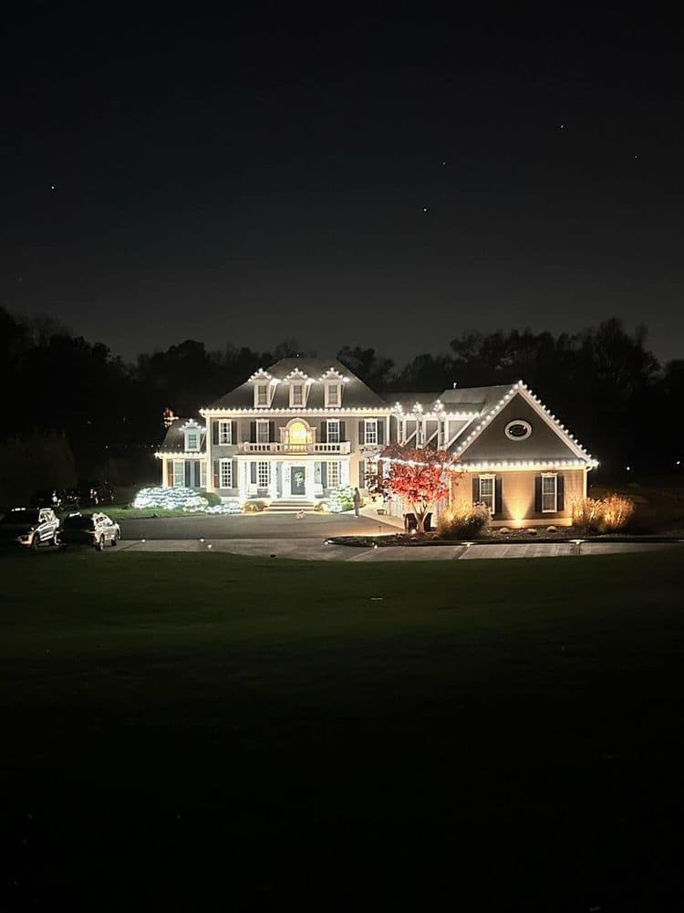 Elegant illuminated house at night with holiday decorations and a spacious driveway.