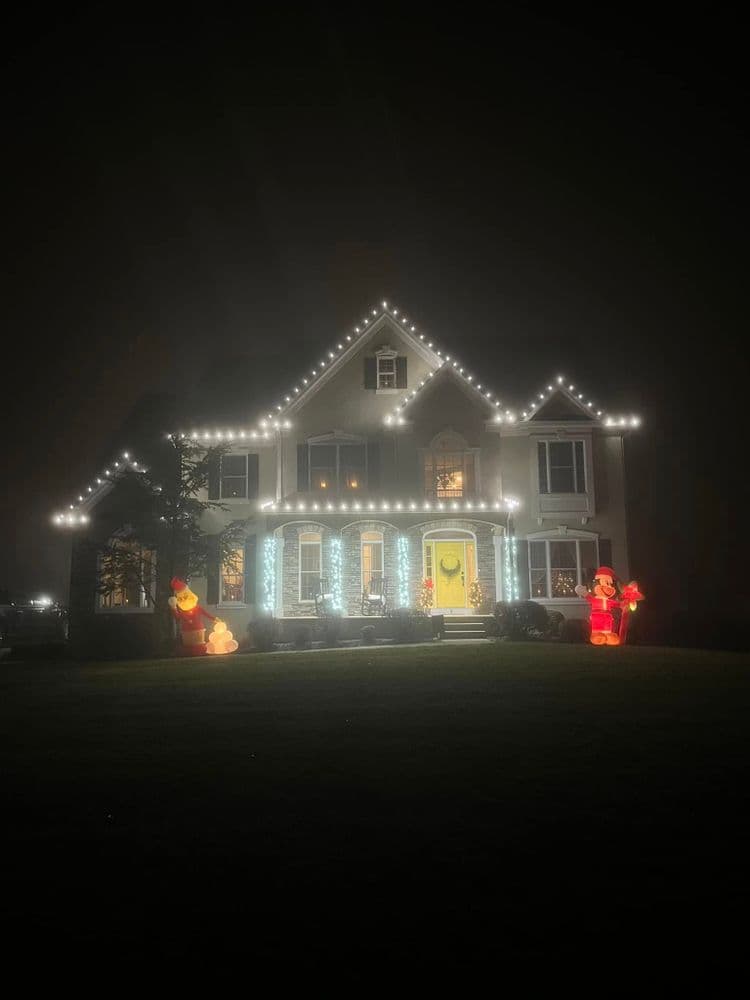 Christmas-decorated house with festive lights and inflatable Santa figures at night.