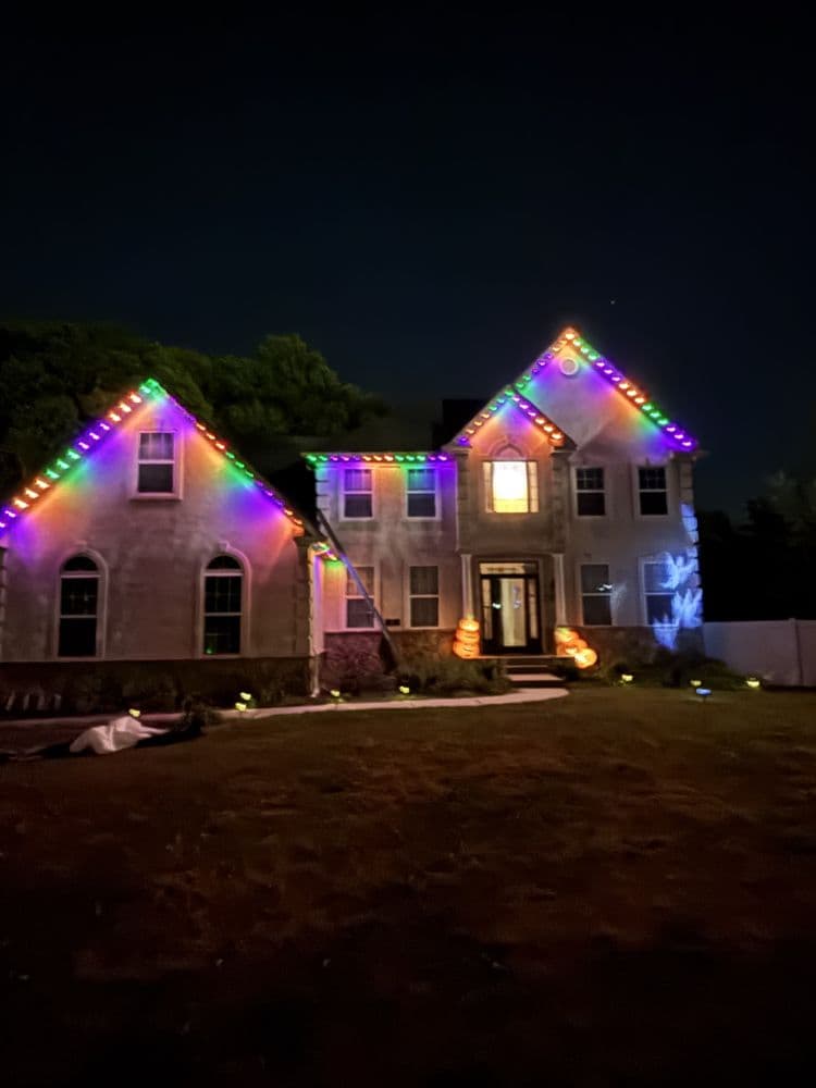 Colorful Halloween lights adorn a house at night, creating a festive atmosphere.