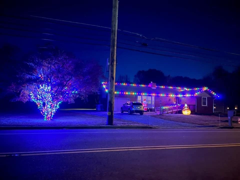 House decorated with colorful Christmas lights and a tree, glowing at night.