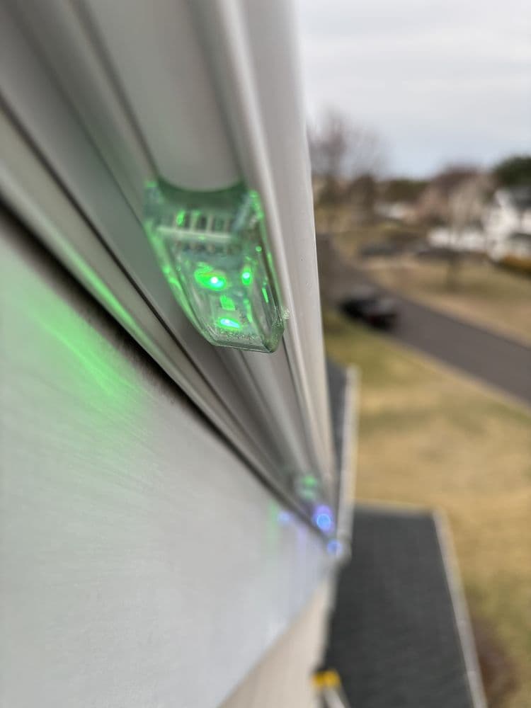 Close-up of holiday lights with green LEDs installed on a house exterior.