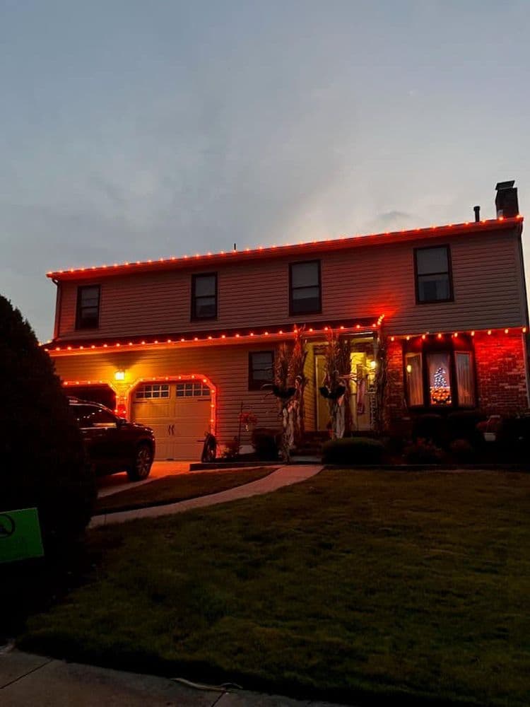 Two-story house decorated with red lights for the holidays, glowing at dusk.