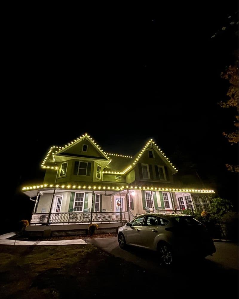 Charming illuminated house at night with festive lights and parked car in front.