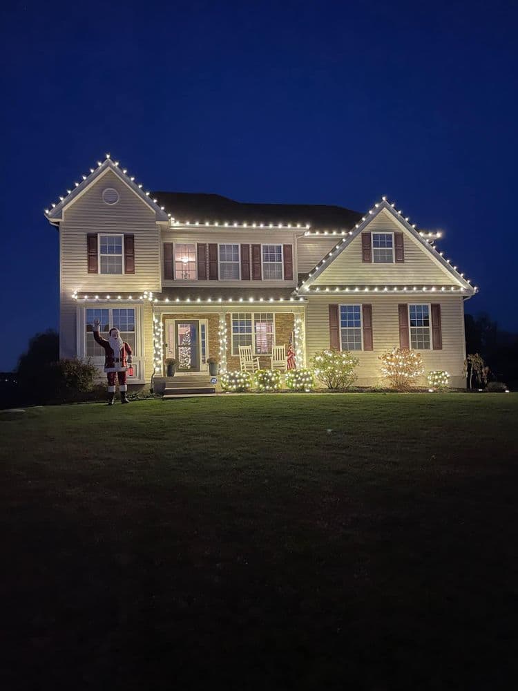 Festively decorated house with Christmas lights and Santa figure on the lawn at night.
