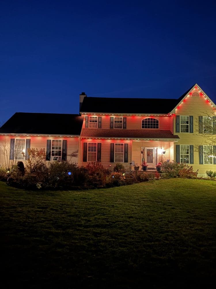 House decorated with red and white lights for the holidays at dusk, surrounded by greenery.