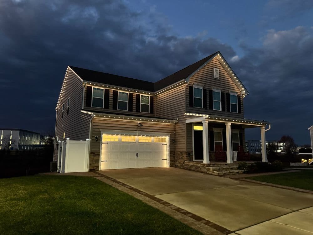Two-story home with festive lights, garage, and lawn under a cloudy evening sky.