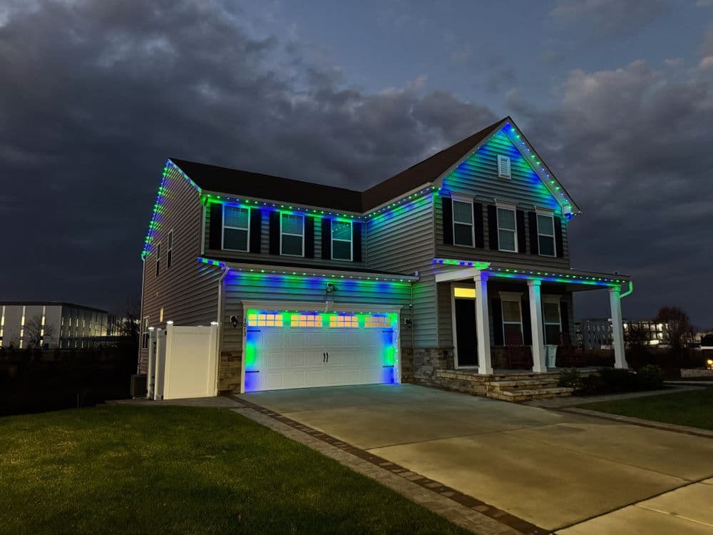 Home adorned with vibrant green and blue holiday lights against a twilight sky.