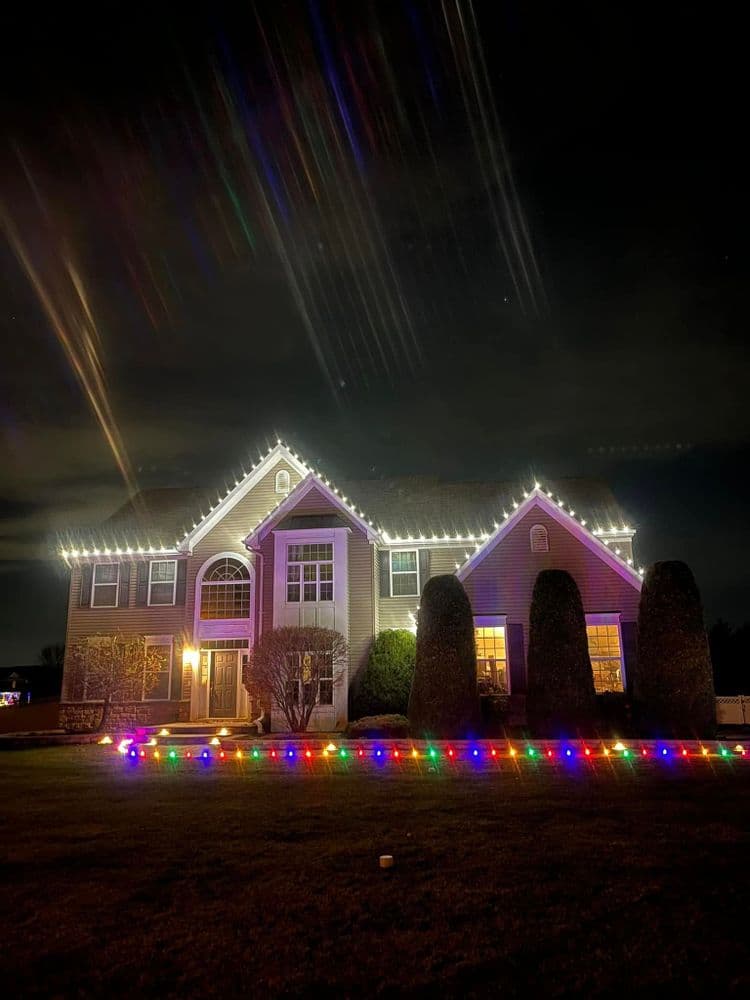Colorful holiday lights adorn a two-story house, creating a festive nighttime scene.