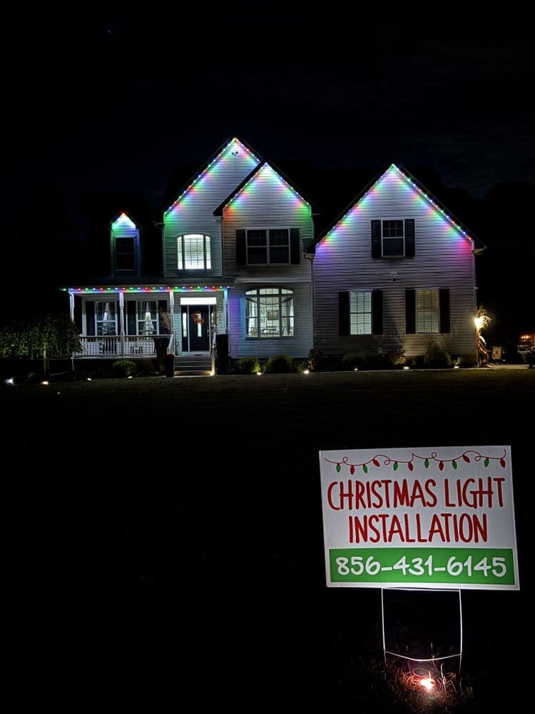 Decorated house with Christmas lights at night and installation service sign.