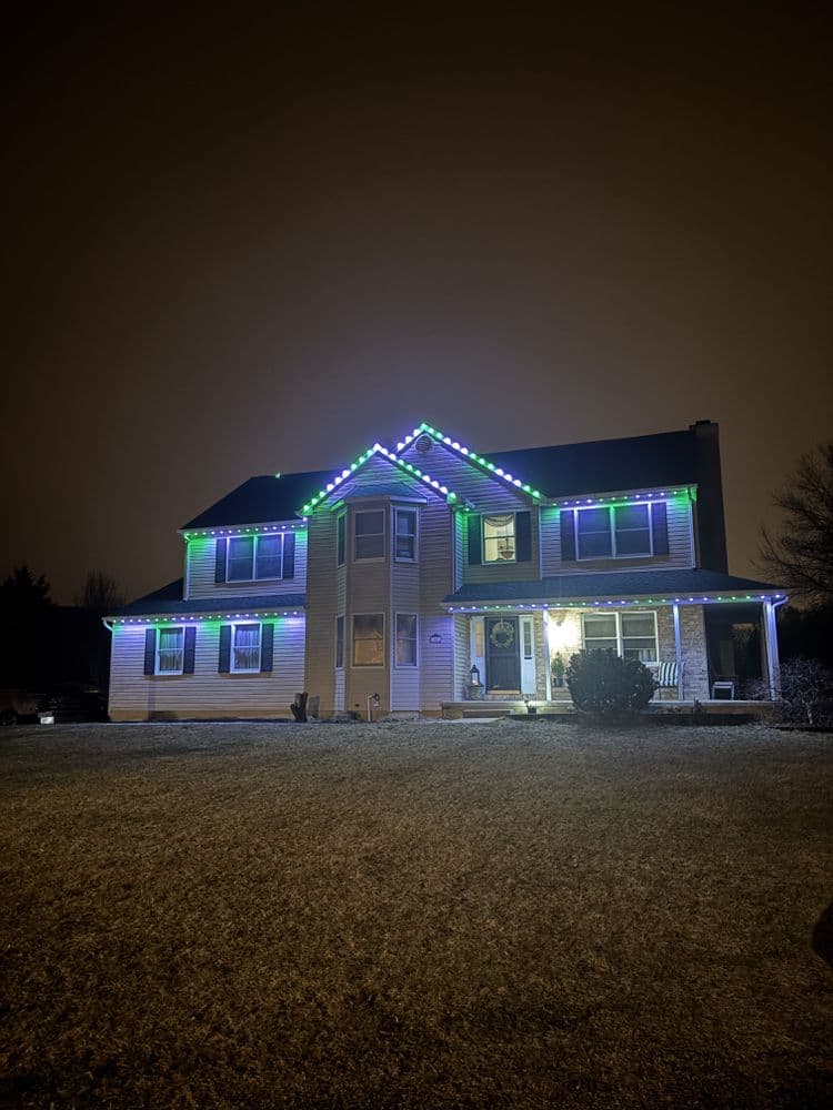 Modern house adorned with vibrant blue and green holiday lights at night.
