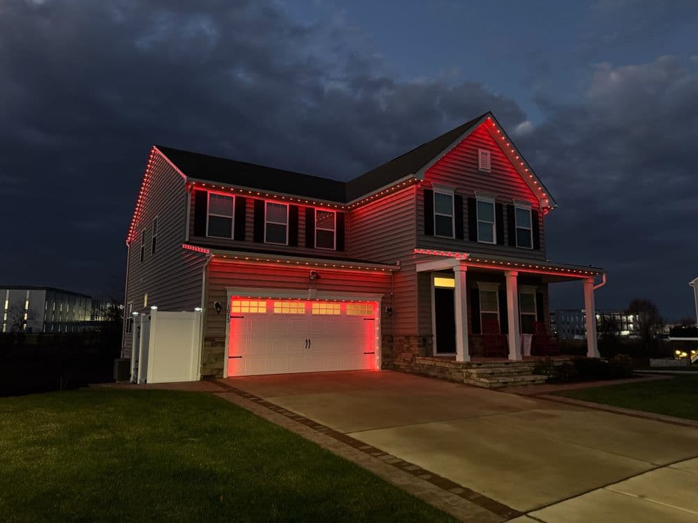 Two-story house decorated with red lights, dark sky, and driveway.