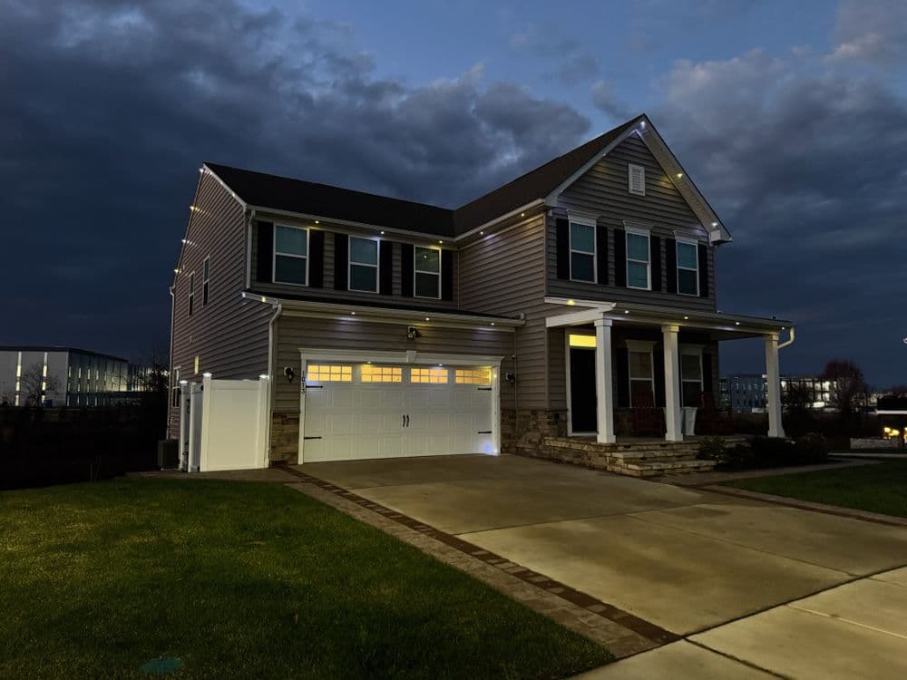 Two-story house with outdoor lighting at dusk, featuring a garage and front porch.