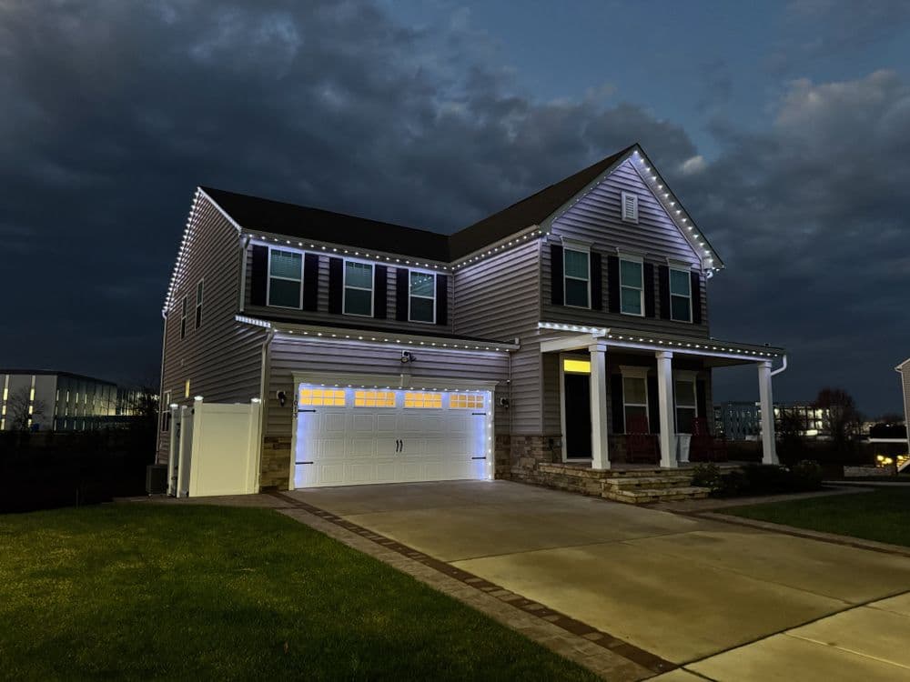 Two-story modern home with decorative outdoor lighting at dusk. Grassy front lawn and driveway.