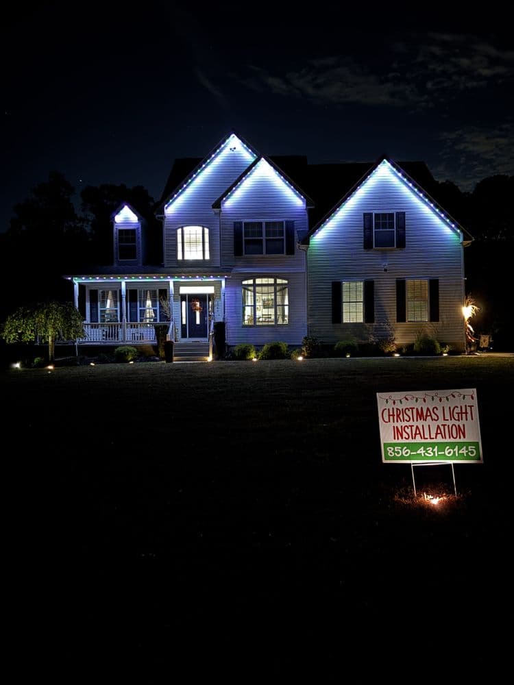 Home with festive blue Christmas lights and a sign for light installation services.