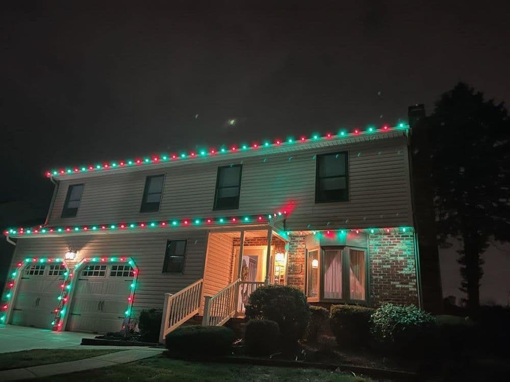 Two-story house decorated with red and green Christmas lights at night.