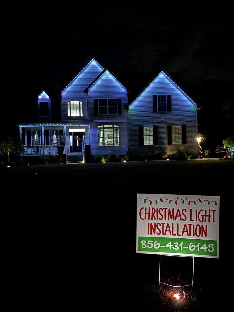 Christmas light installation on a beautifully decorated home at night with a contact sign.