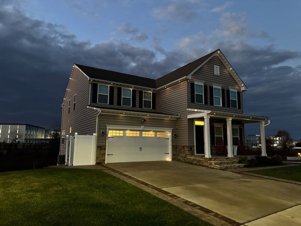 Modern two-story house with exterior lights at dusk, showcasing manicured lawn and driveway.