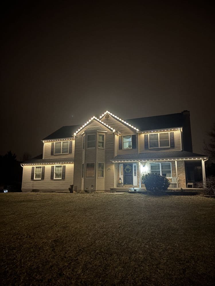 Two-story house illuminated with festive lights on a dark night.