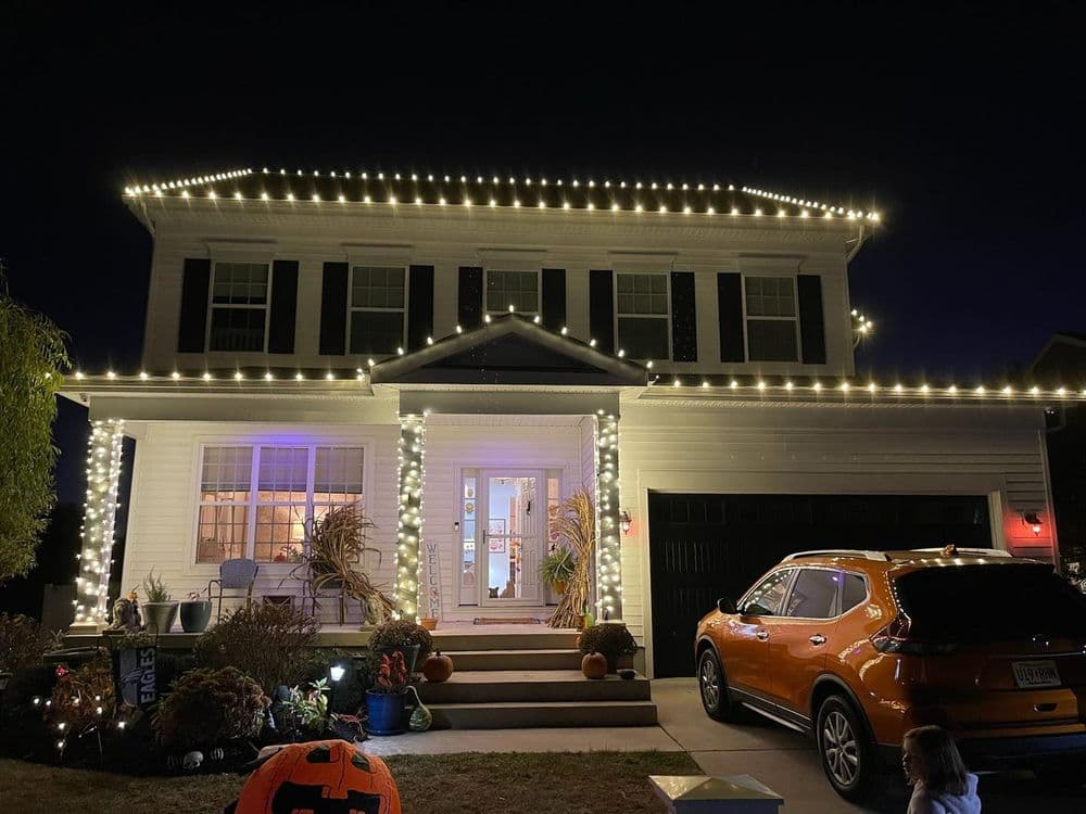Two-story house decorated with string lights for Halloween, with a pumpkin in the yard.