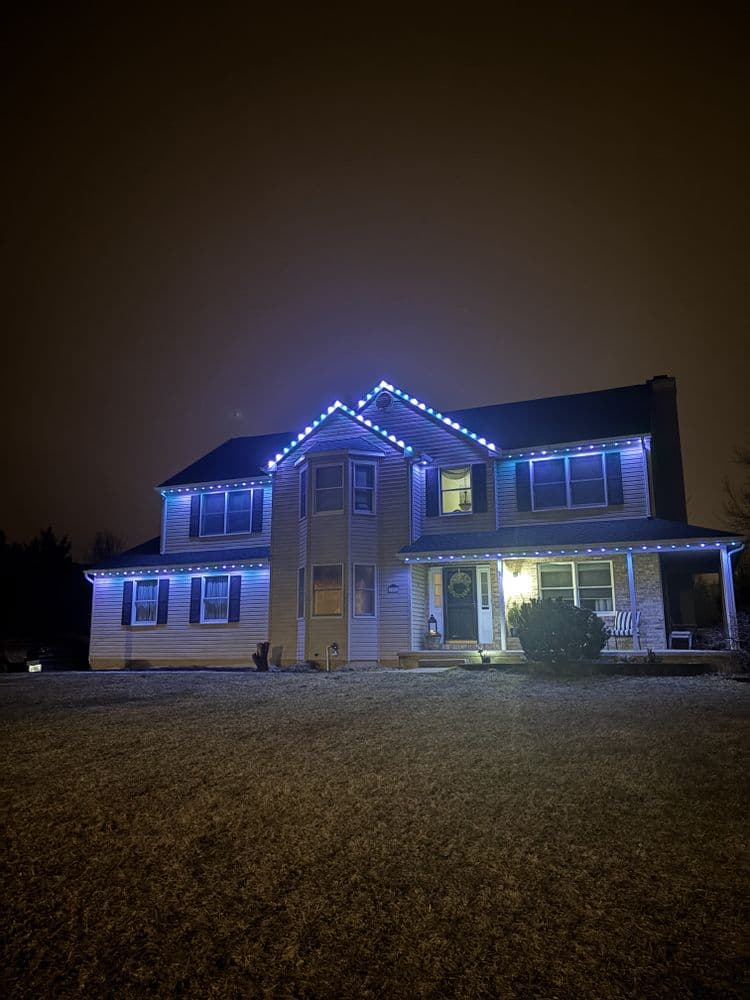 Two-story house decorated with blue lights for the holiday season at night.