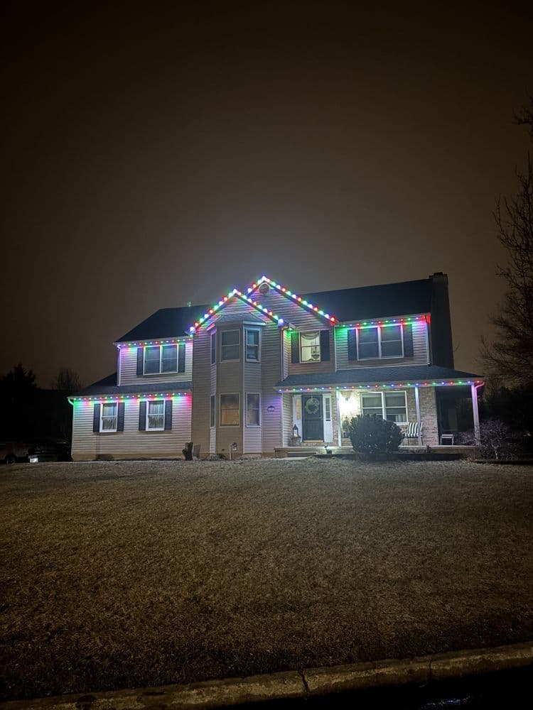 House decorated with colorful Christmas lights on a foggy night. Front lawn visible.