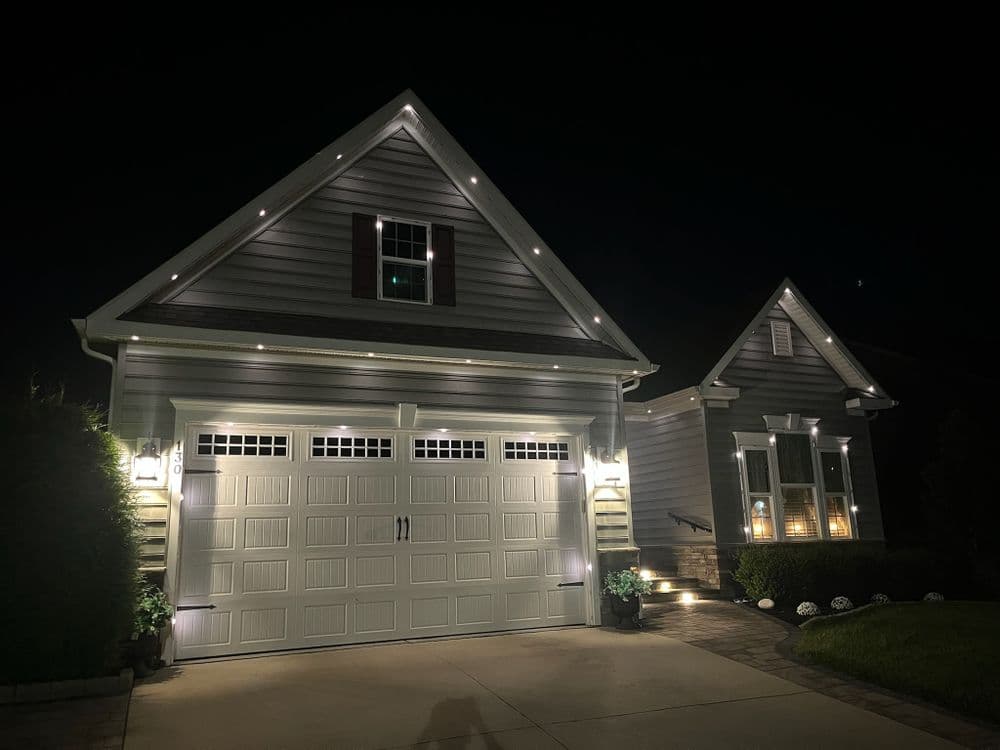Modern house at night with illuminated garage, landscaped entrance, and elegant lighting.