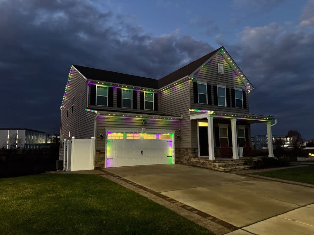 Festively lit modern house at dusk with colorful lights along roof and garage.