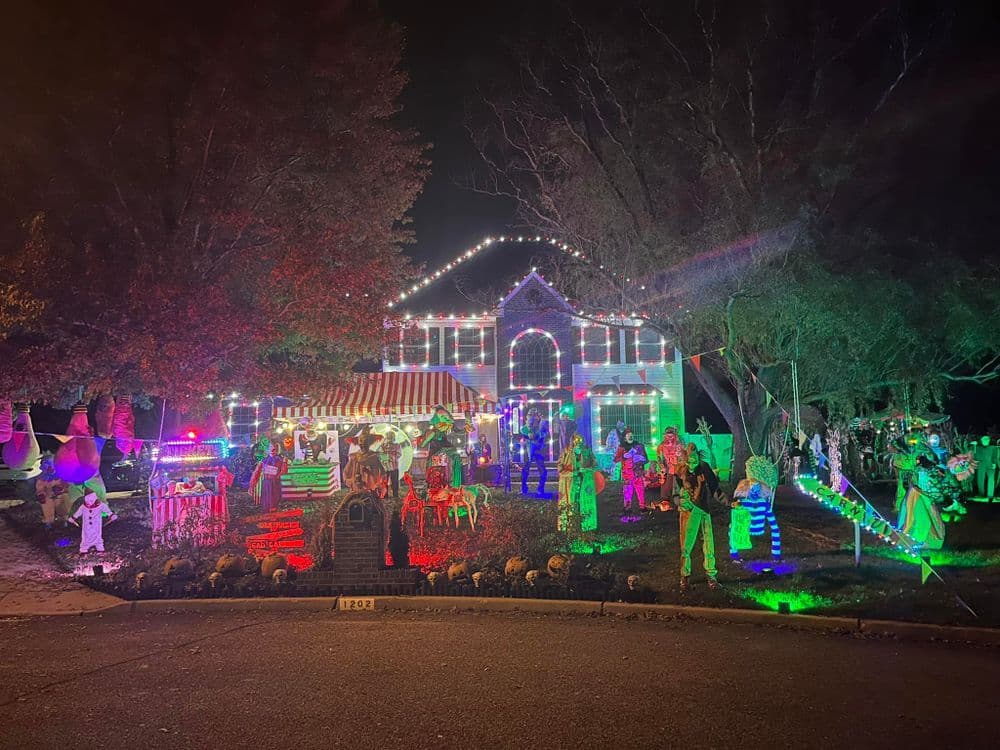 Festively decorated house with colorful lights and Halloween figures at night.