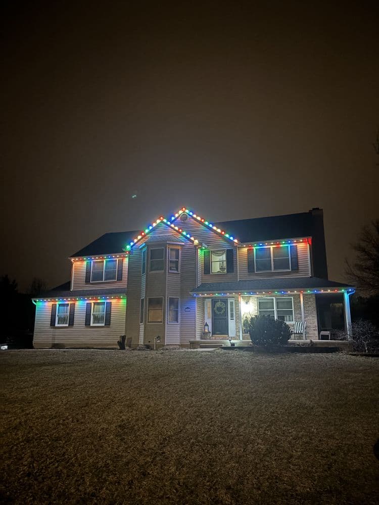 Colorful holiday lights adorn a two-story house at night, creating a festive atmosphere.