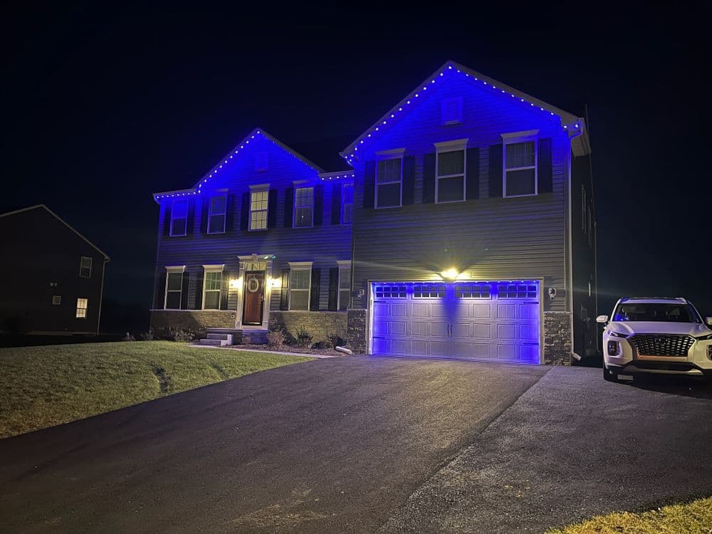 Modern house illuminated with blue lights at night, featuring a two-car garage and lawn.