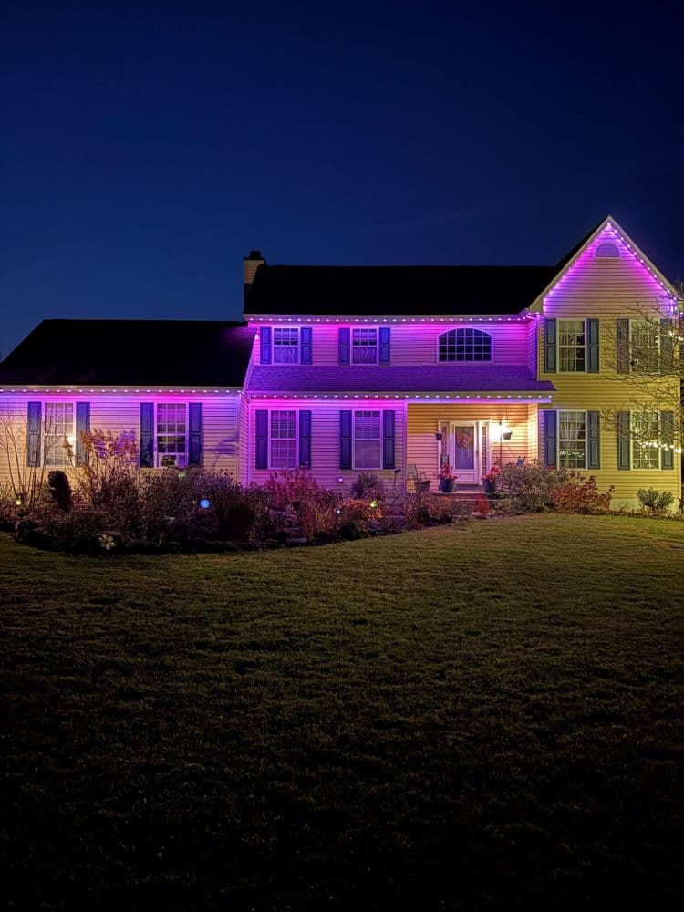 Purple LED lights adorn a two-story house, creating a festive night scene.