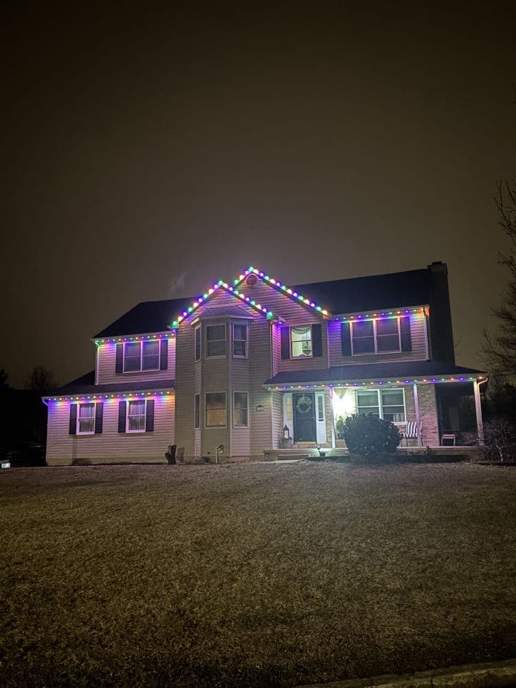 Festively lit pink house with colorful lights on roof, glowing at night.