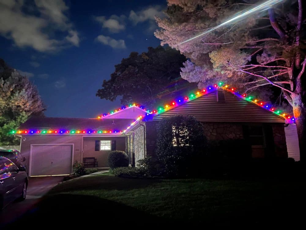 House decorated with colorful holiday lights at night, surrounded by trees.