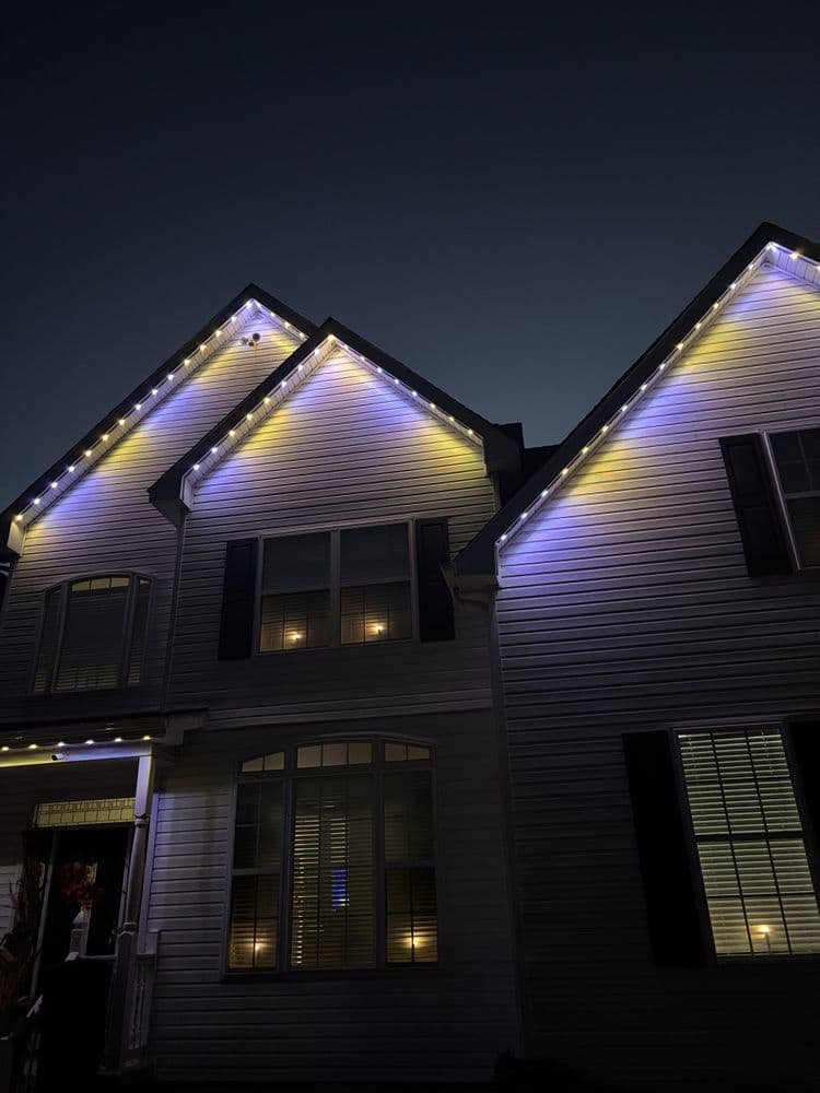 Modern home with purple and white decorative lights on roof during nighttime.