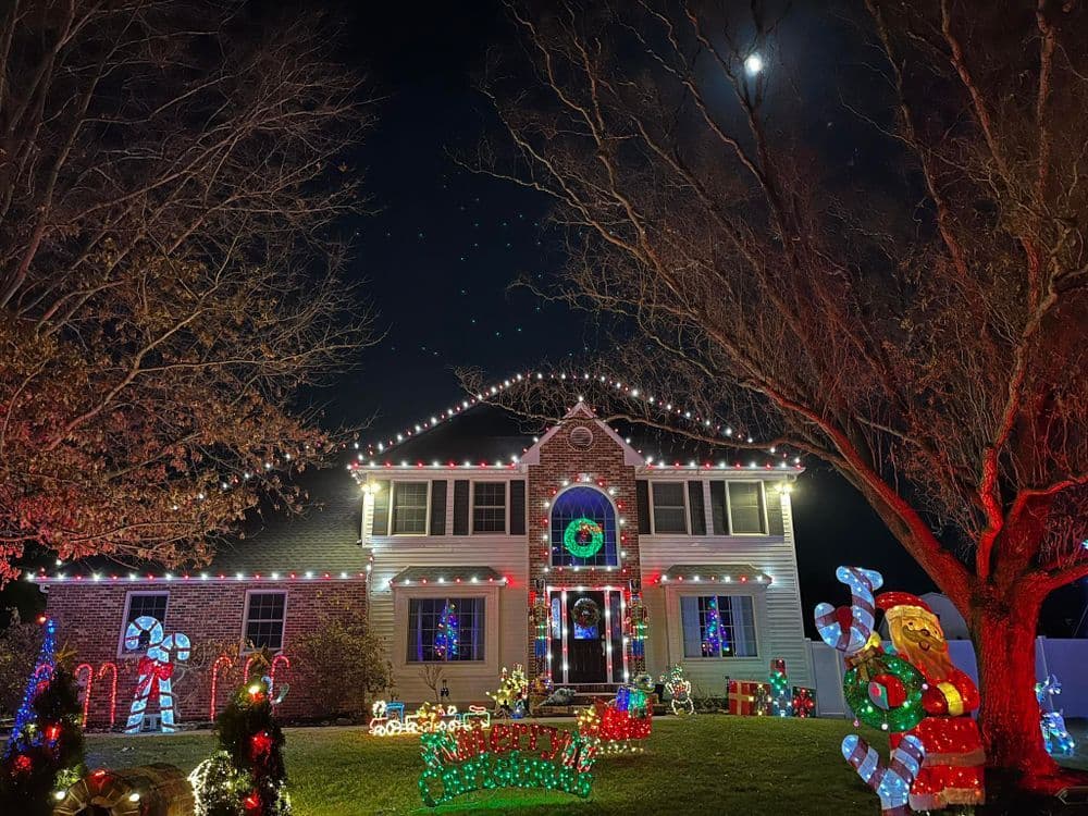 Festively illuminated house with Christmas lights and decorations under a moonlit sky.