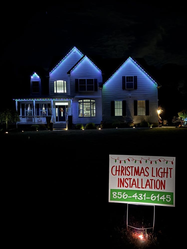 Holiday lights adorning a house with a sign for Christmas light installation services.