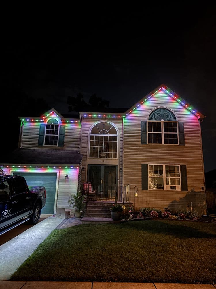 Festively lit house at night with colorful holiday lights along the roofline.