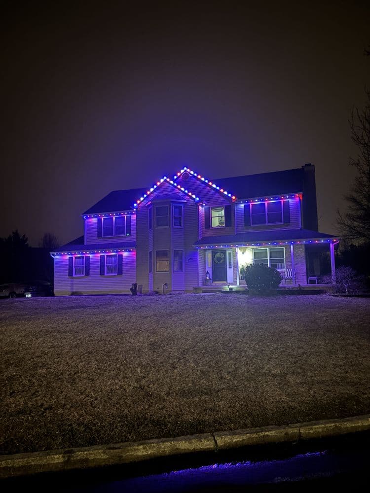 Decorated house with colorful purple and blue lights on a dark, rainy night.